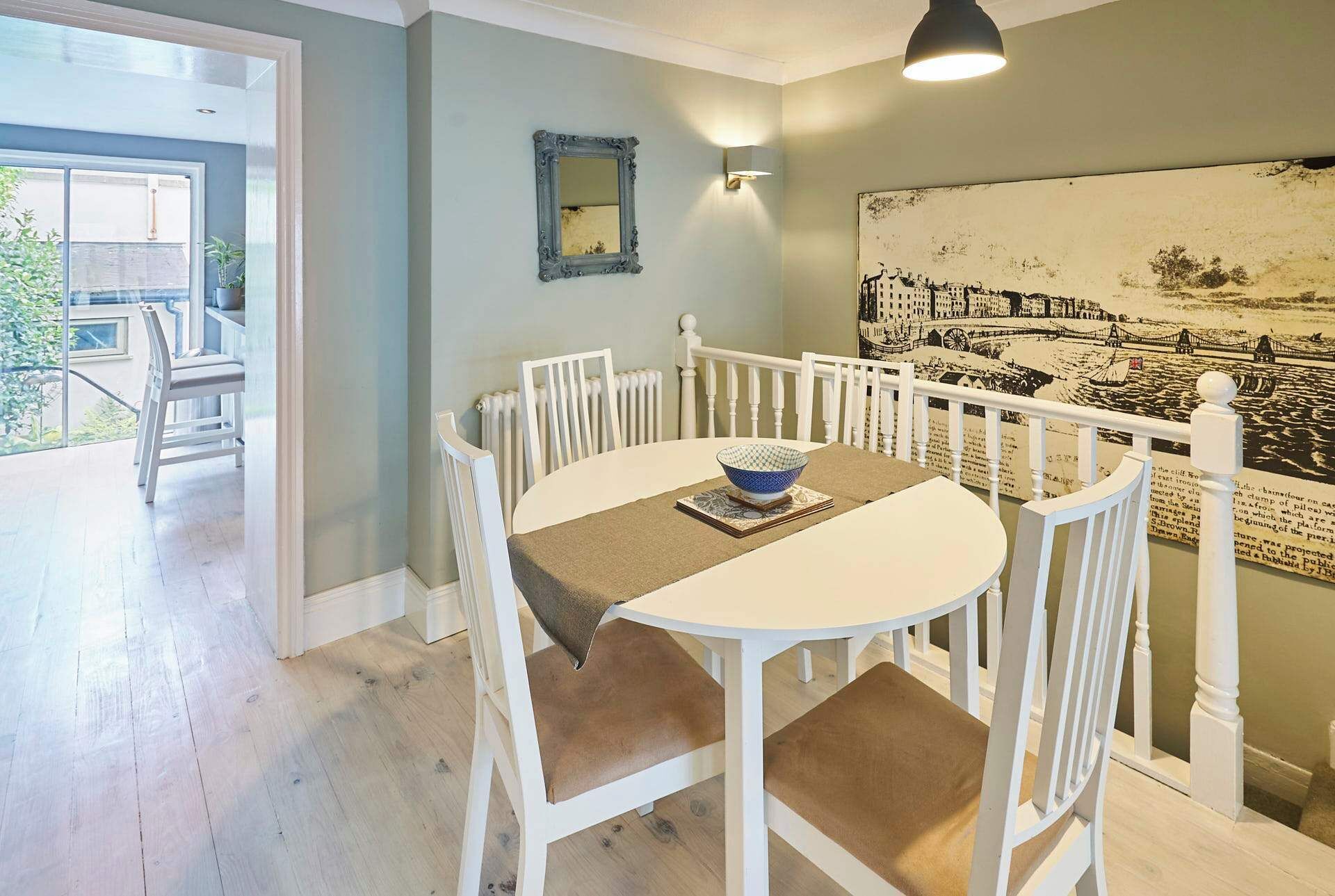 A dining area with a round table, white chairs, a bowl, and a wall-mounted lamp.
