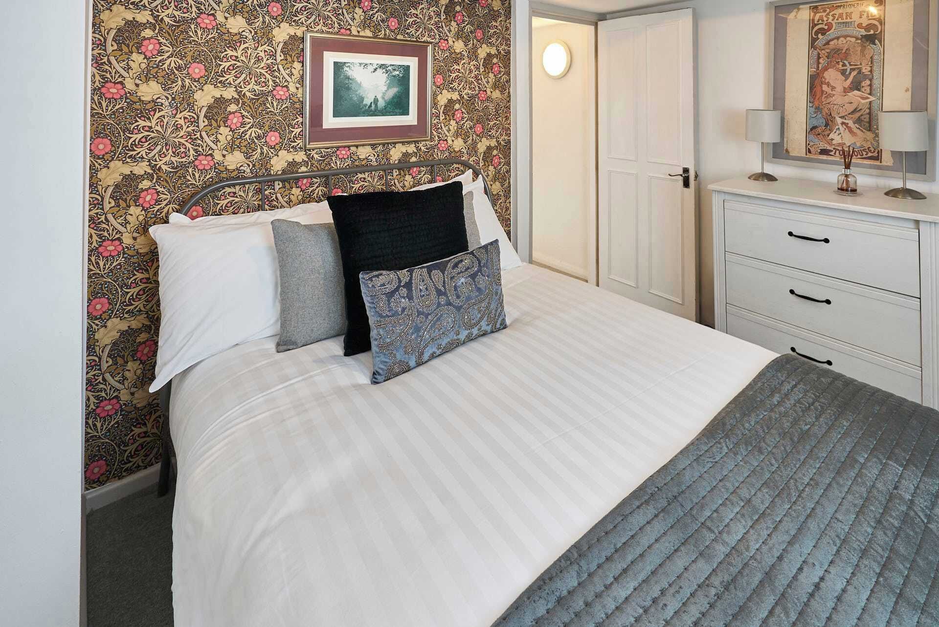 A neatly made bed with a patterned pillow, a bedside table with a lamp, and a door leading to another room.