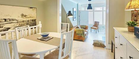 A dining area with a white table and chairs, a bowl on the table, and a staircase leading to another room.