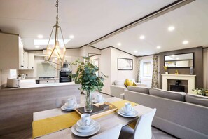 A modern living room with a dining area, a sofa set, a fireplace, and a kitchen in the background. - Host Stay Sunbird Lodge (York)