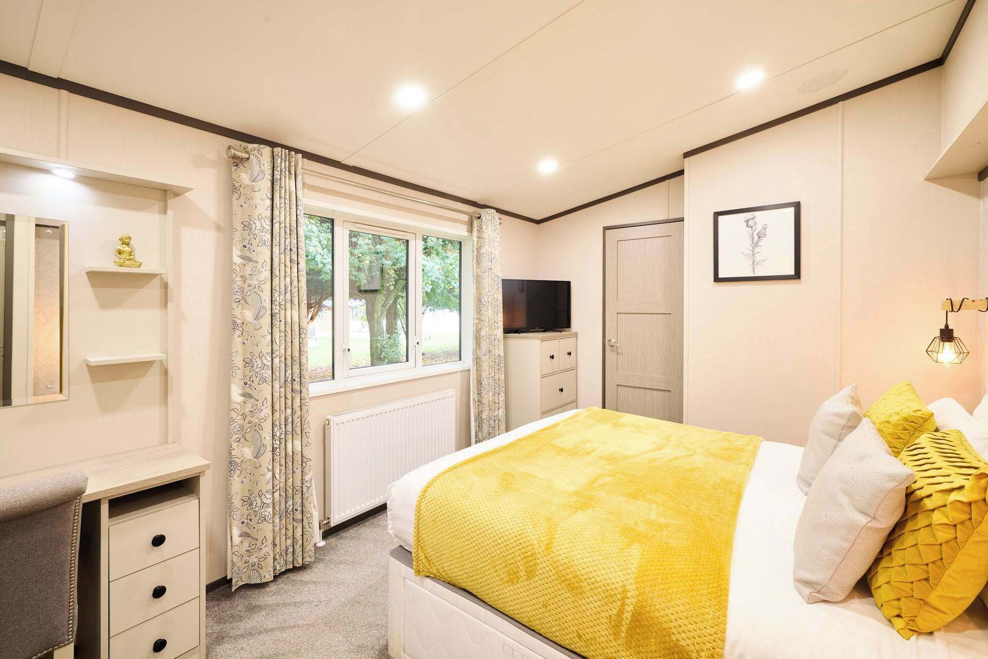 A bedroom with a bed, a TV, a desk, and a window.