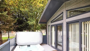 En moderne udendørs terrasse med jacuzzi, et overdækket siddeområde og en glasdør, der fører til en træterrasse.