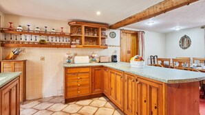 A kitchen with wooden cabinets, a countertop, and a dining area with chairs. - Host Stay Windles (Wotton-under-Edge)