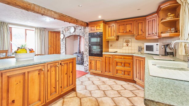 A kitchen with wooden cabinets, a stone archway, a microwave, and a sink. - Host Stay Windles (Wotton-under-Edge)