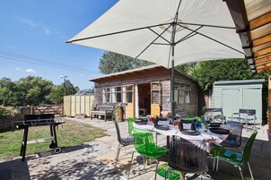 Un patio al aire libre con una mesa lista para comer, rodeada de sillas y una barbacoa.
