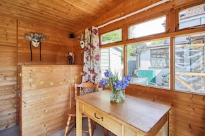 A wooden cabin interior with a wooden desk, a chair, a vase with flowers, and a window with curtains. - Host Stay Windles (Wotton-under-Edge)