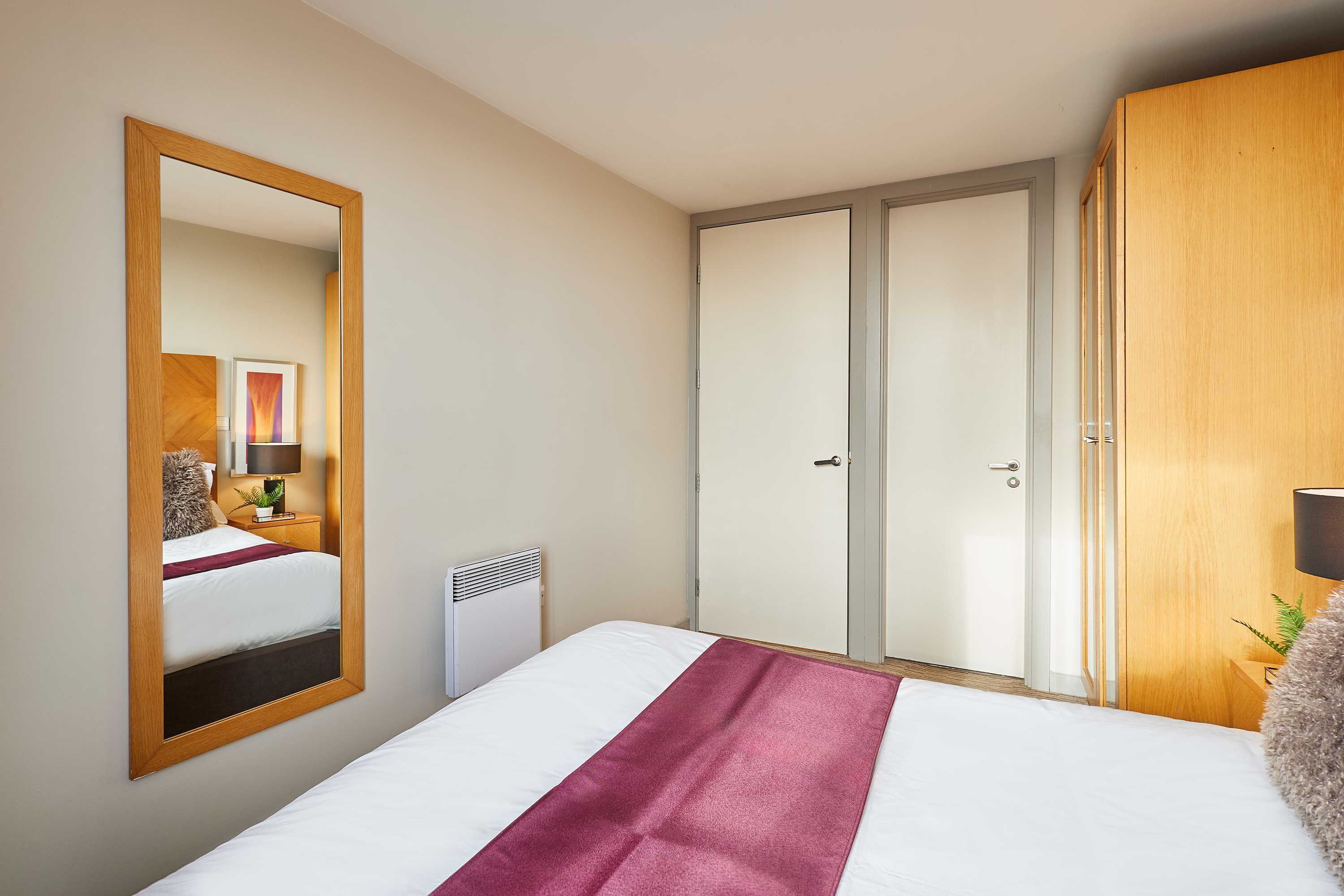 Ein Hotelzimmer mit einem Bett, einem Schrank, einem Spiegel und einem Nachttisch mit einer Lampe.
