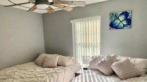 Een slaapkamer met twee bedden, een plafondventilator, een raam met zonwering en een schilderij aan de muur.