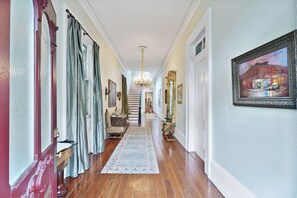 Ein Korridor mit Holzboden, einem Chandelier, einer Treppe und einem Gemälde an der Wand.