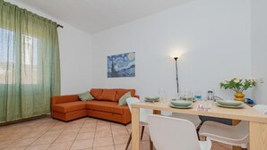 Uma sala de estar com sofá, uma mesa de jantar com cadeiras, um quadro na parede e um abajur.
