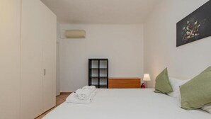 Quarto de hotel com cama, mesa de cabeceira, luminária, quadro e guarda-roupa.