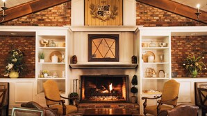A cozy living room with a fireplace, wooden shelves, and leather chairs. - Pine Needles Lodge & Golf Club (Southern Pines)