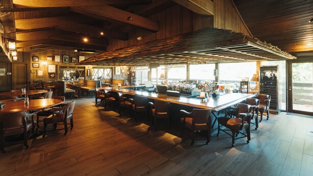 A spacious bar area with wooden flooring and high ceilings, featuring a long counter with stools and a variety of seating options. - Pine Needles Lodge & Golf Club (Southern Pines)