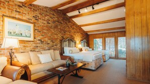 A cozy room with a brick wall, wooden beams, a sofa, a bed, and a window with blinds. - Pine Needles Lodge & Golf Club (Southern Pines)