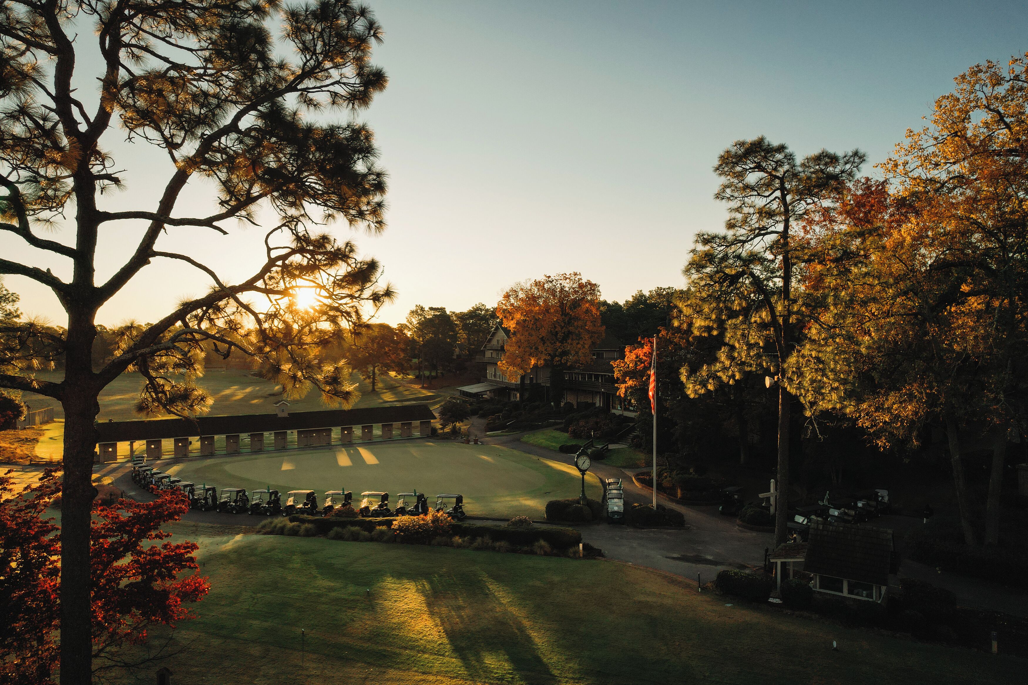 Un campo de golf con un club house, rodeado de árboles y un cielo despejado.