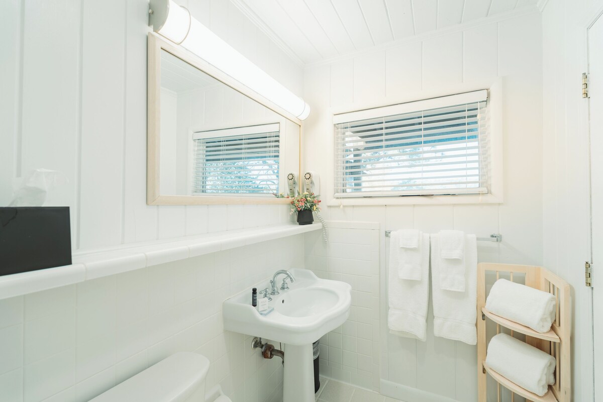 A bathroom with a white sink, a mirror, and a window with blinds.