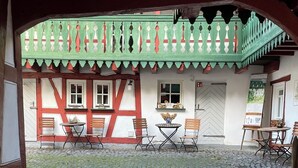 A courtyard with cobblestone flooring, a green balcony with white trim, and a traditional building with wooden beams and white walls. - Stylish time out in the Hunsrück - views and comfort (Herrstein)