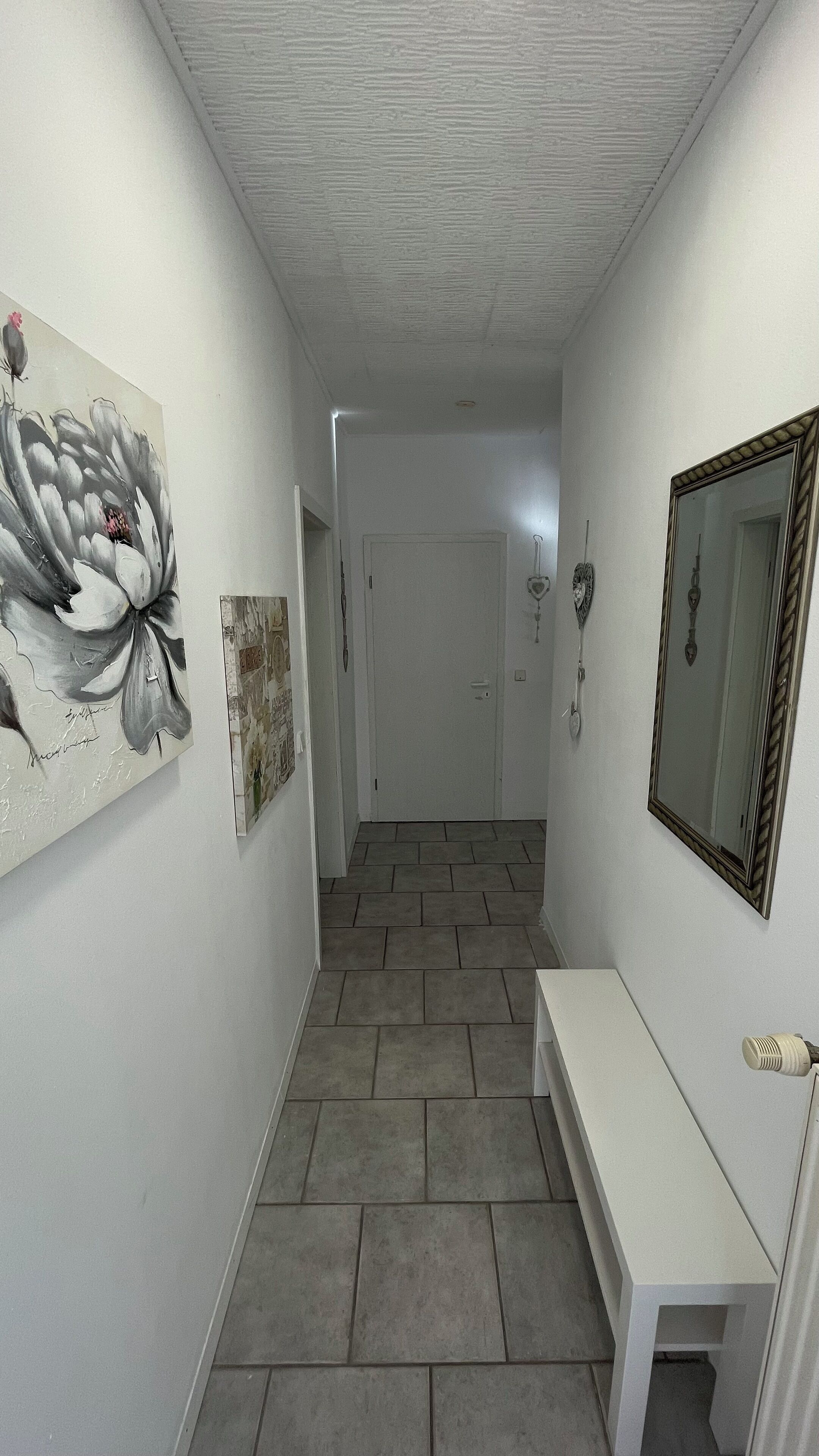 A hallway with a white bench, a mirror, and artwork on the walls.