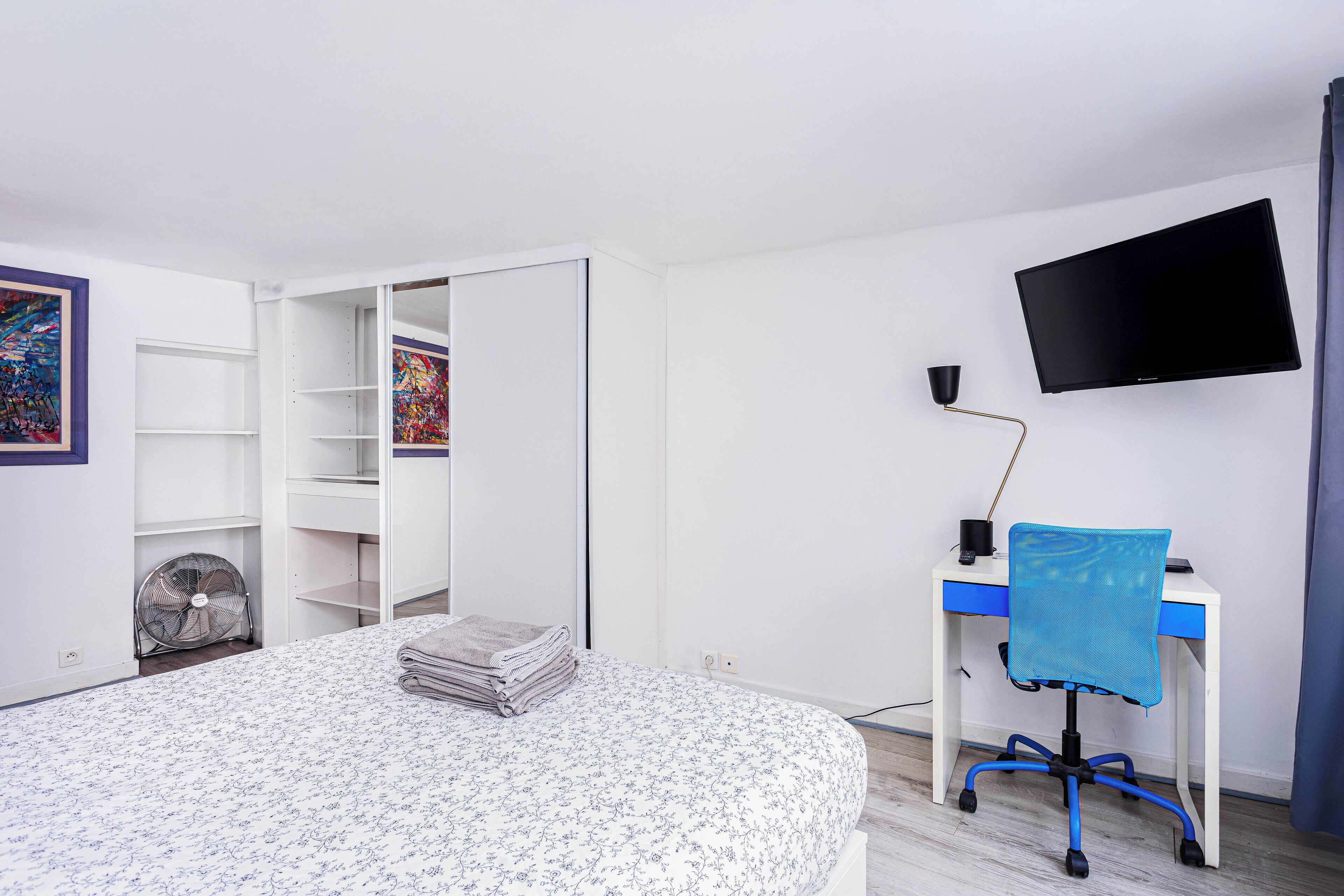 A bedroom with a bed, a desk with a chair, a TV, and a wardrobe.