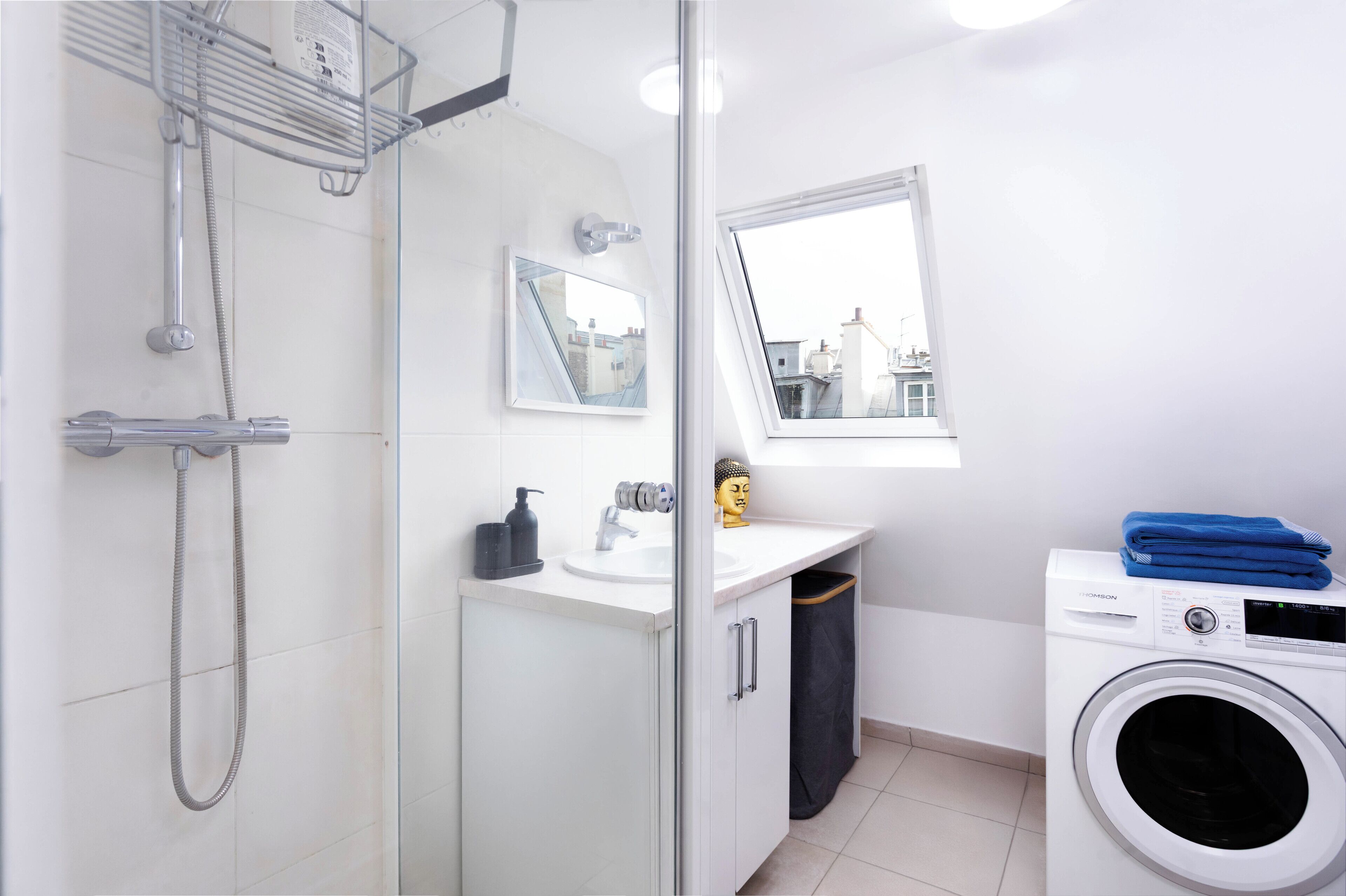 Un baño moderno con cabina de ducha de vidrio, lavamanos con espejo, ventana con vistas y lavadora.