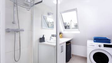 Un baño moderno con cabina de ducha de vidrio, lavamanos con espejo, ventana con vistas y lavadora.