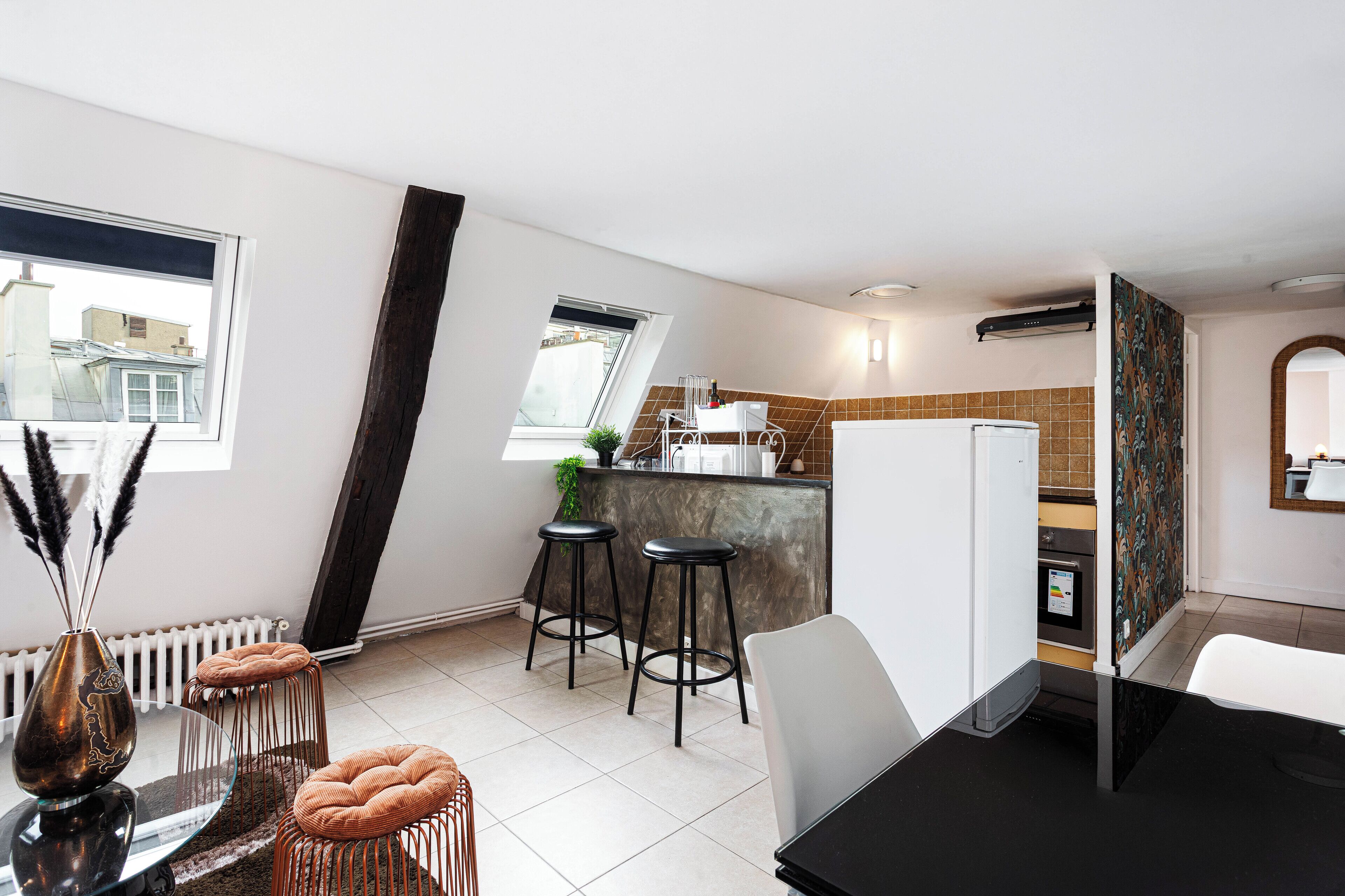 Une cuisine compacte comprenant un coin repas, un radiateur et une fenêtre donnant sur des immeubles.