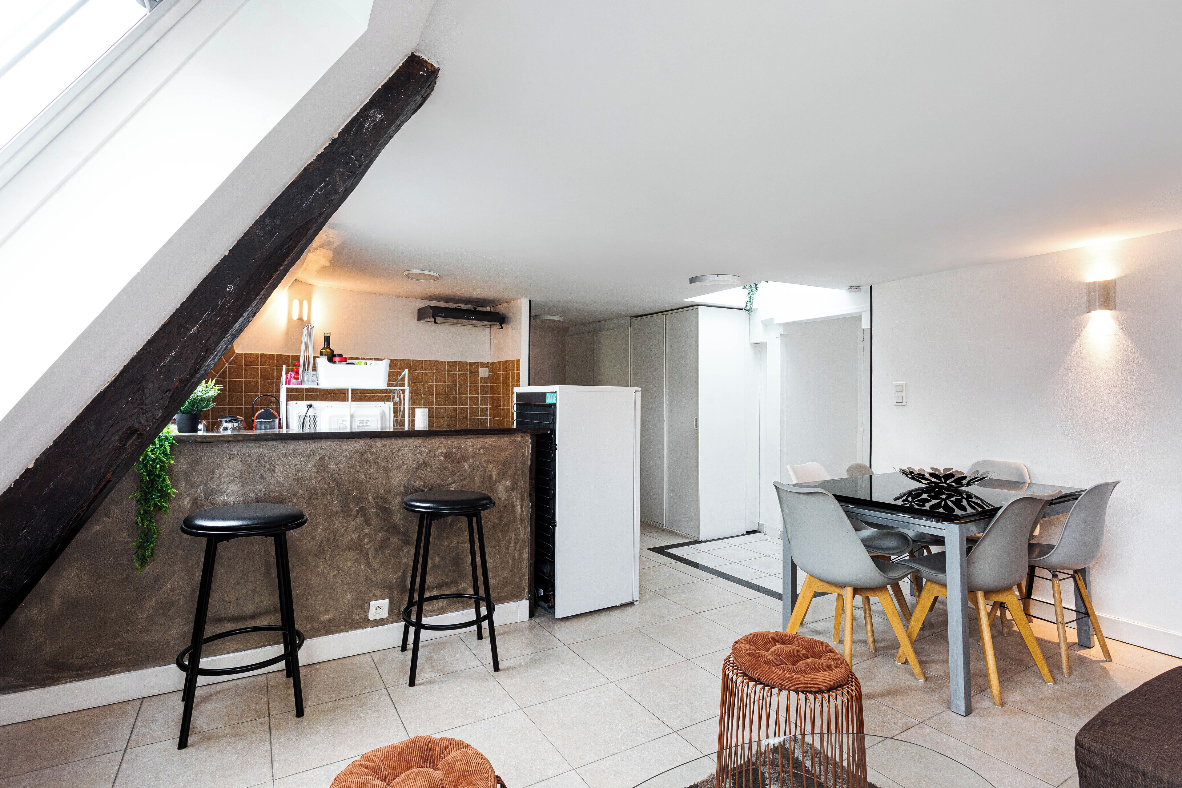 Una cocina moderna con comedor, que incluye una isla de cocina con taburetes, una mesa de comedor con sillas y una escalera con una viga de madera oscura.