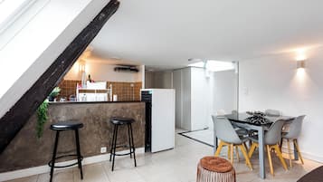 Una cocina moderna con comedor, que incluye una isla de cocina con taburetes, una mesa de comedor con sillas y una escalera con una viga de madera oscura.