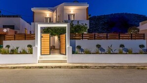 Uma casa moderna de dois andares, com entrada bem iluminada, cerca de madeira e jardim ajardinado.