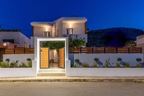Una casa moderna de dos pisos con una entrada iluminada, un cerco de madera y un jardín ajardinado.