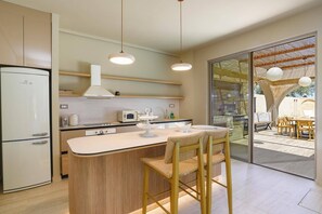 Eine moderne Küche mit integriertem Kühlschrank, Mikrowelle und Herd. Durch eine Glastür ist ein Essbereich mit Tisch und Stühlen zu sehen.