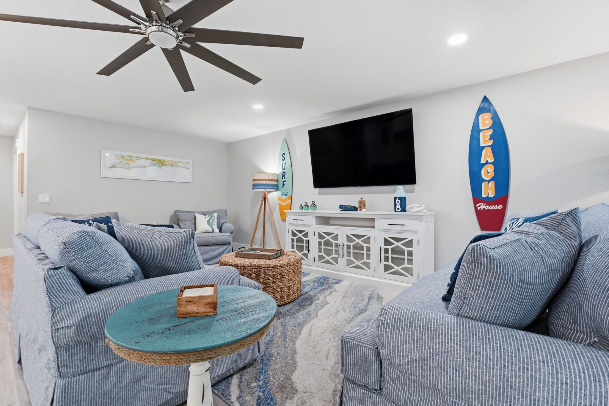 Una sala de estar con ventilador de techo, televisor, decoración de tabla de surf y muebles a rayas.