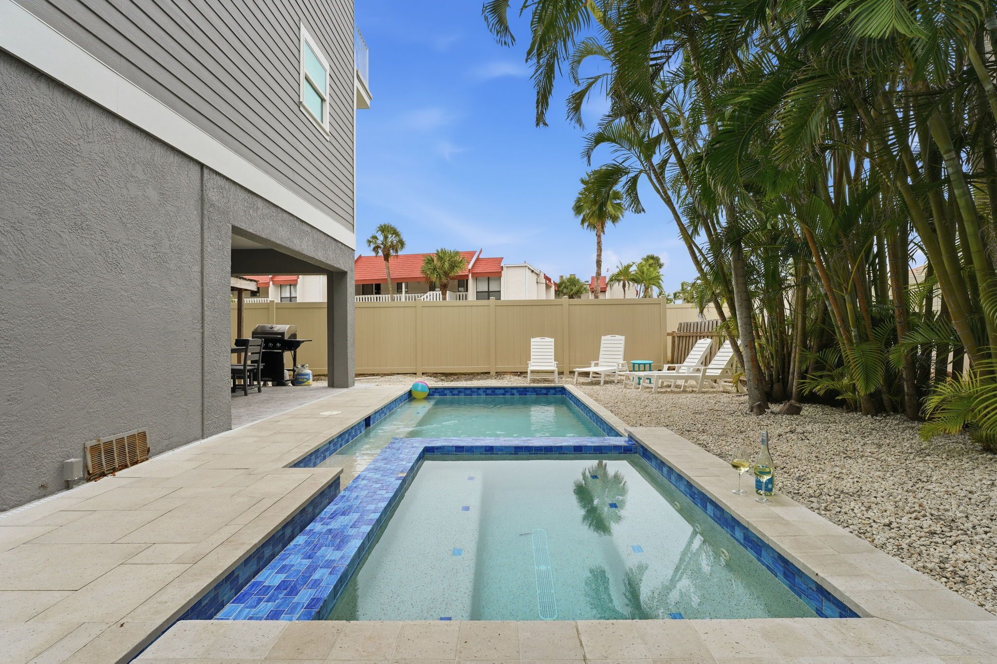 Une piscine dont le bord est revêtu de carrelage, entourée d’une terrasse aménagée avec des chaises et une table.