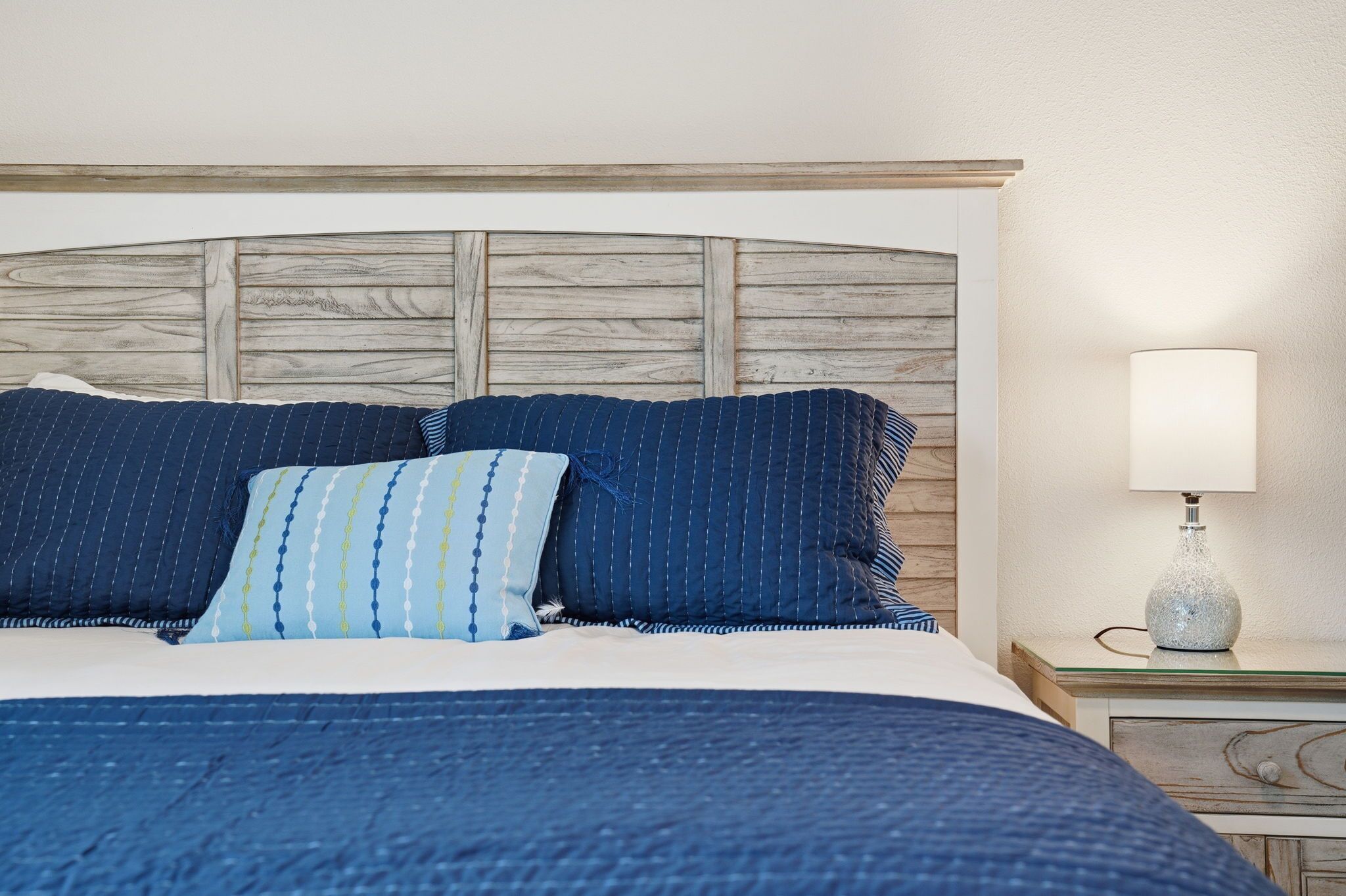A bed with a wooden headboard, blue bedding, and a bedside lamp.