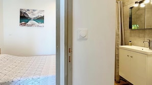 A bedroom with a bed, a painting of a mountain landscape, and a bathroom with a sink and mirror. - Apartment 4 people - sea view - Théoule sur mer (Côte d'azur) - ESQUILLON (Théoule-sur-Mer)