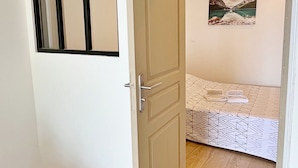 Ein Zimmer mit Holzboden, einem Bett mit gemusterten Bettwaren, einer Tür mit Fenster und einem Gemälde an der Wand.