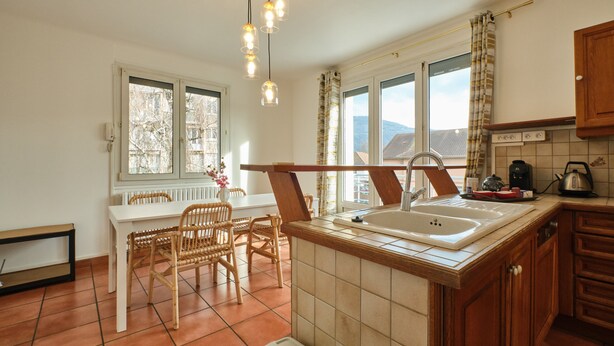 A kitchen with a white countertop, wooden cabinets, a sink, and a dining area with chairs and a table.