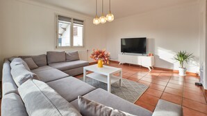 A modern living room with a sectional sofa, a flat-screen TV, a white coffee table, and a potted plant.