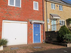 A two-story residential building with a red brick facade, a white garage door, and a blue front door. - Harbour Way (Shoreham-by-Sea)