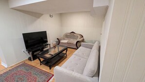 Een woonkamer met een flatscreen televisie, een bank, een tweezitterbank en een salontafel.