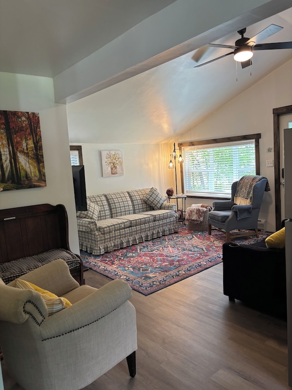 A living room with a ceiling fan, a sofa, a chair, a rug, and a window with blinds.