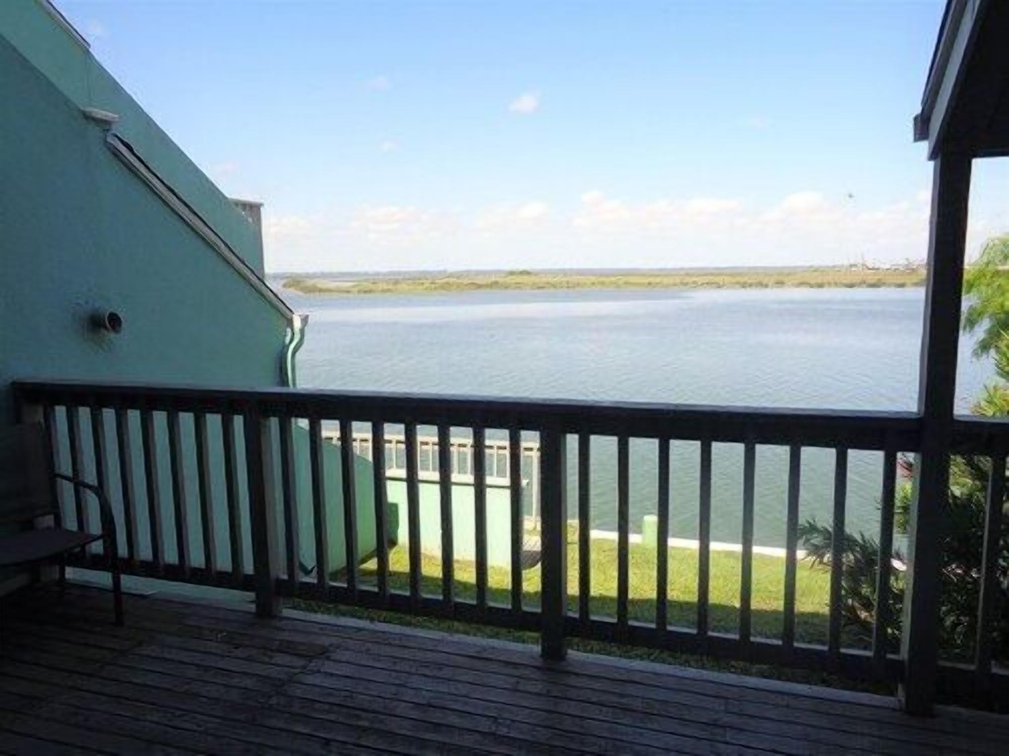 A wooden deck with a railing overlooking a calm body of water and a distant shoreline.