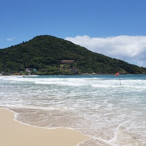 Una playa con olas, una montaña al fondo y un edificio de varios pisos.