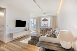 Ein modernes Wohnzimmer mit Flachbildfernseher, einer Couch, einem Couchtisch und einer Lampe.