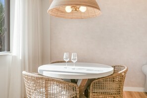 Une table ronde, deux verres à vin, des chaises en osier disposées autour, le tout sous un luminaire tressé.