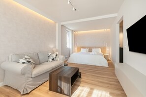Ein modernes Hotelzimmer mit einer Couch, einem Holztisch, einem Bett mit weißer Bettwäsche und einem an der Wand montierten Fernseher.
