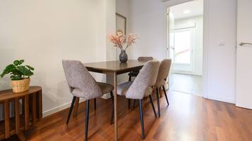 A dining area with a wooden table, four grey upholstered chairs, a vase with flowers, and a wicker basket with a plant.