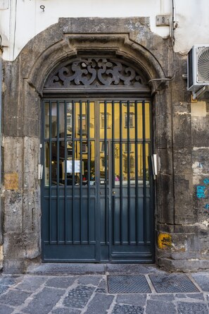 Un cancello in metallo nero con arco decorativo, incastonato in un muro di pietra con una targa numerica.