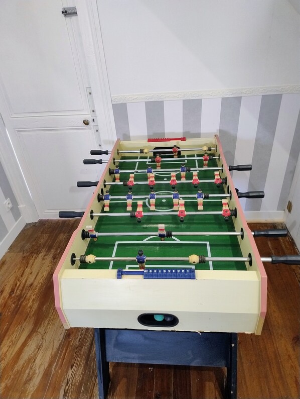 Una mesa de fútbol de mesa en una habitación con piso de madera y paredes blancas.