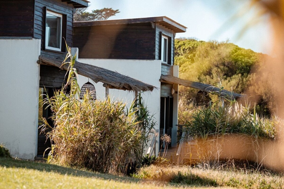 A two-story building with a white exterior and dark trim, surrounded by vegetation.